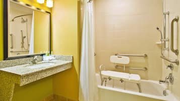 A bathroom with a granite countertop sink, a shower with grab bars, and a white bathtub.