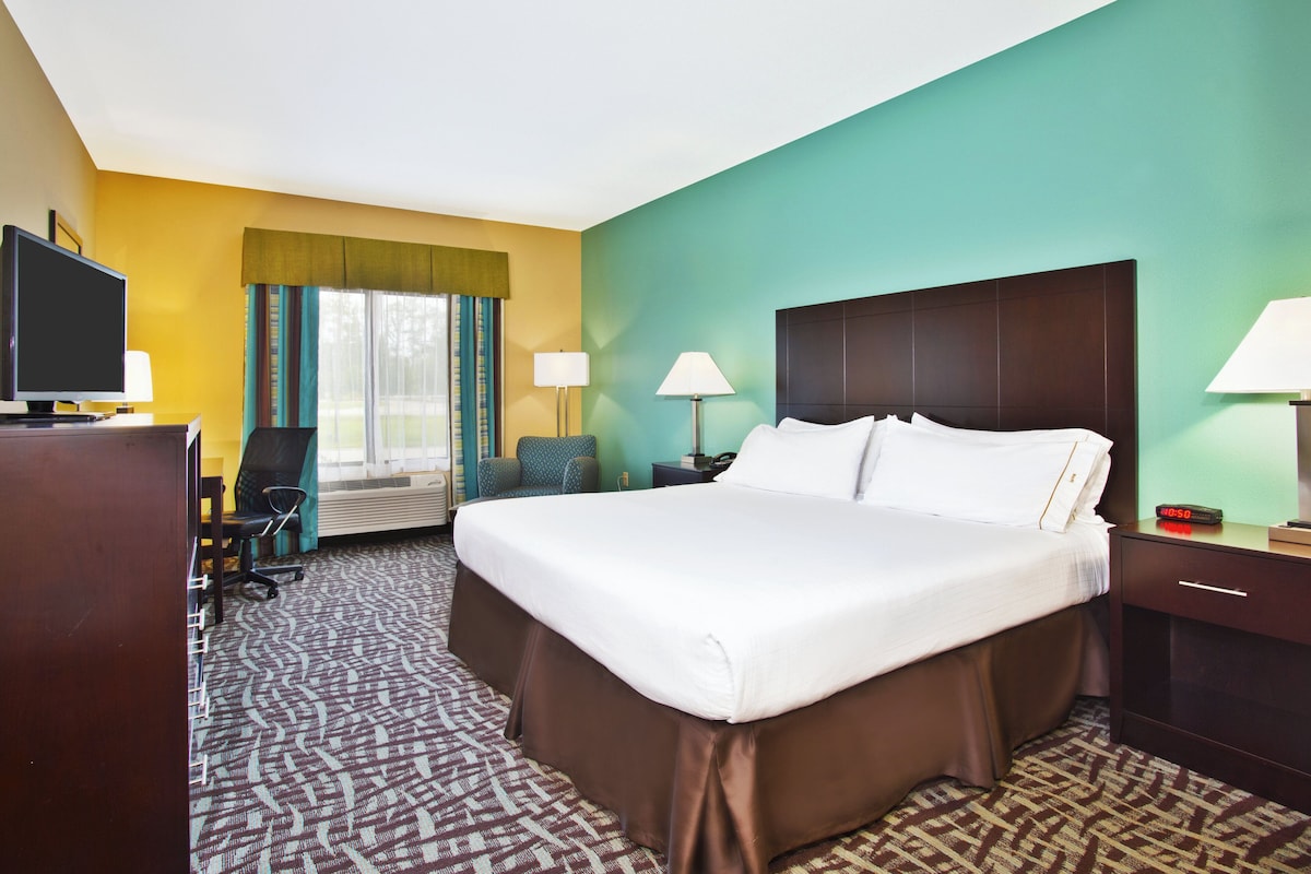 A hotel room with a large bed, two bedside tables, a desk with a chair, a television, and a window with curtains.