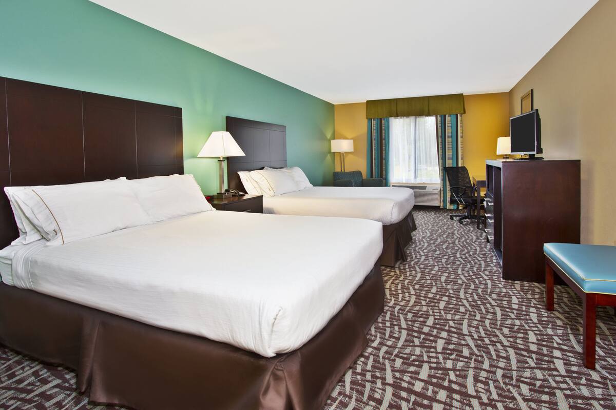 A hotel room with two beds, a desk, a chair, and a television.