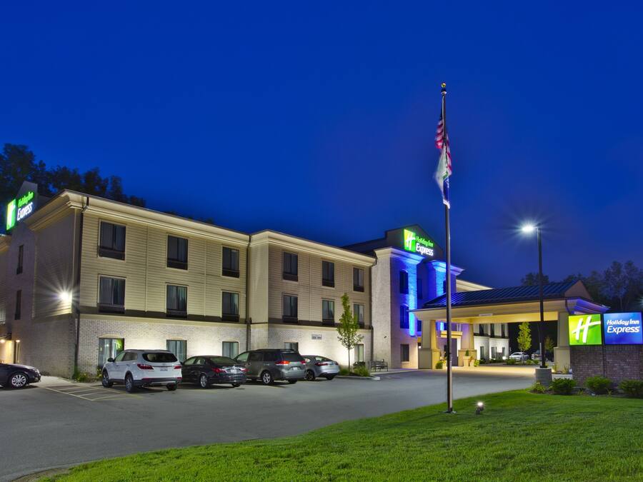 Un hotel Holiday Inn Express con un estacionamiento, un asta de bandera y una entrada bien iluminada.