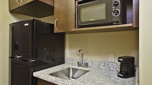 Una cocina con refrigerador de acero inoxidable, microondas integrado, lavamanos de granito y cafetera.