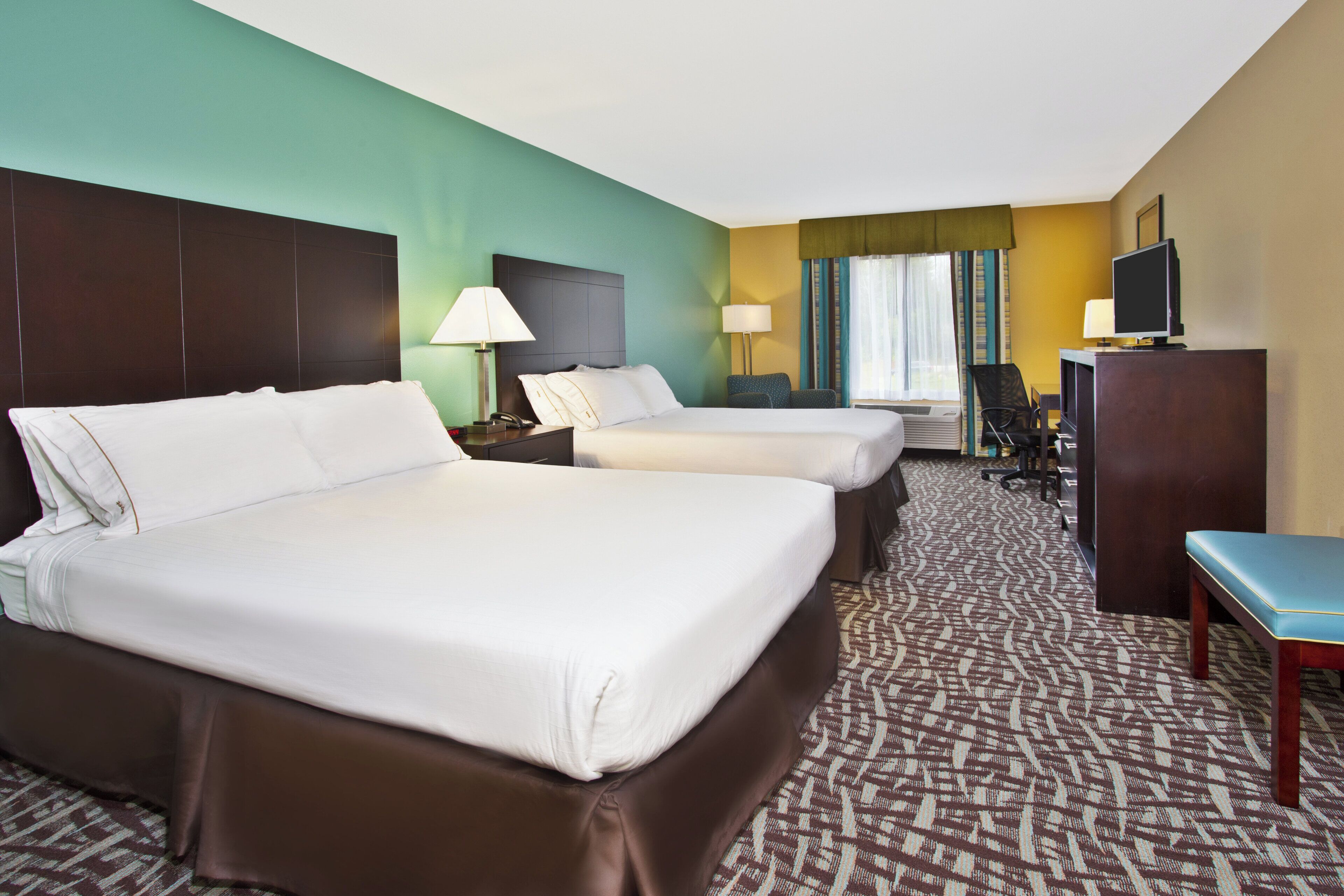 A hotel room with two beds, a desk, a chair, a television, and a window with curtains.