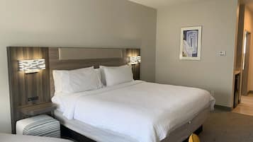 Une chambre d’hôtel avec un grand lit, deux lampes de chevet, une tête de lit ornée d’un motif géométrique, une petite table de chevet, un pouf rayé et un tableau encadré accroché au mur.