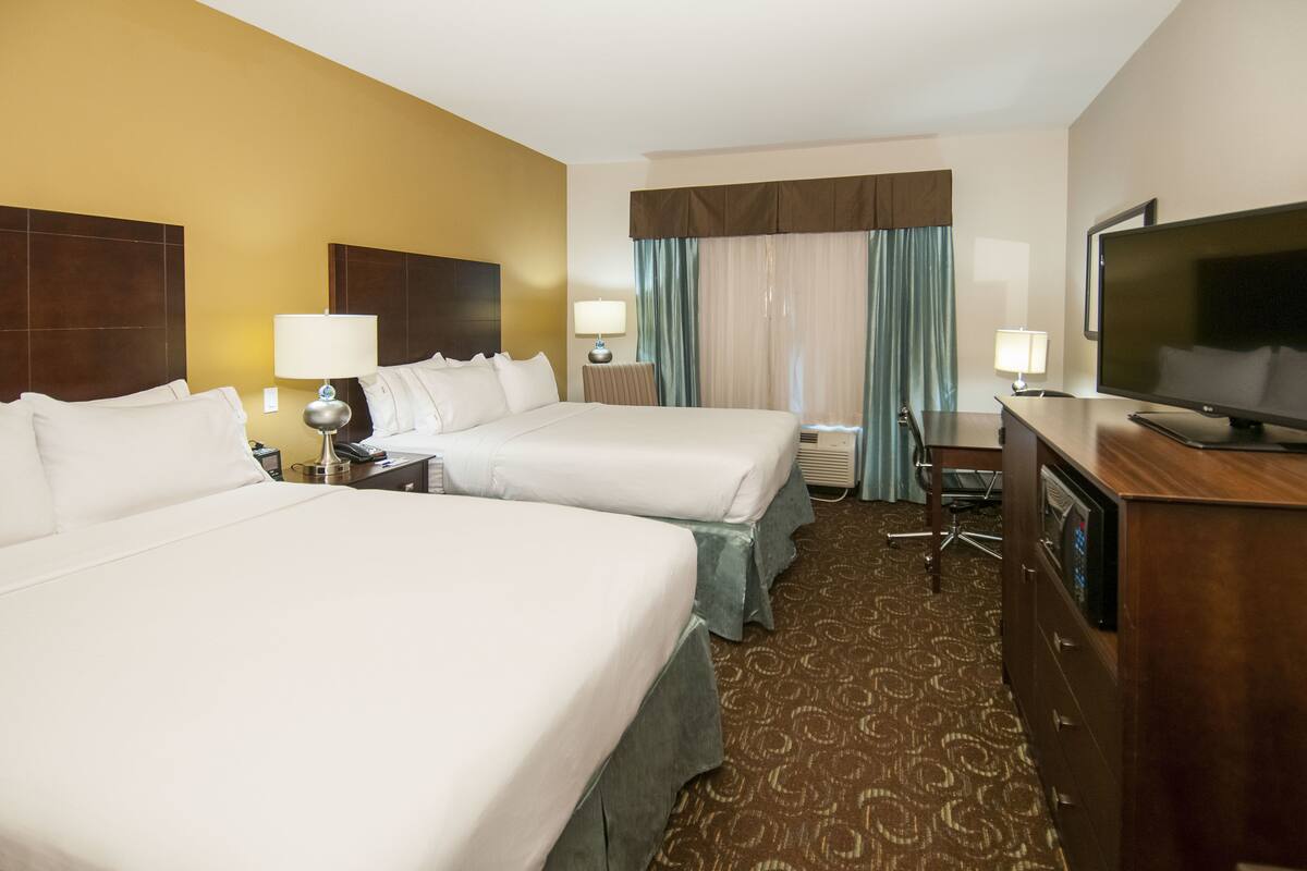 A hotel room with two beds, a desk, a television, and a window with curtains.