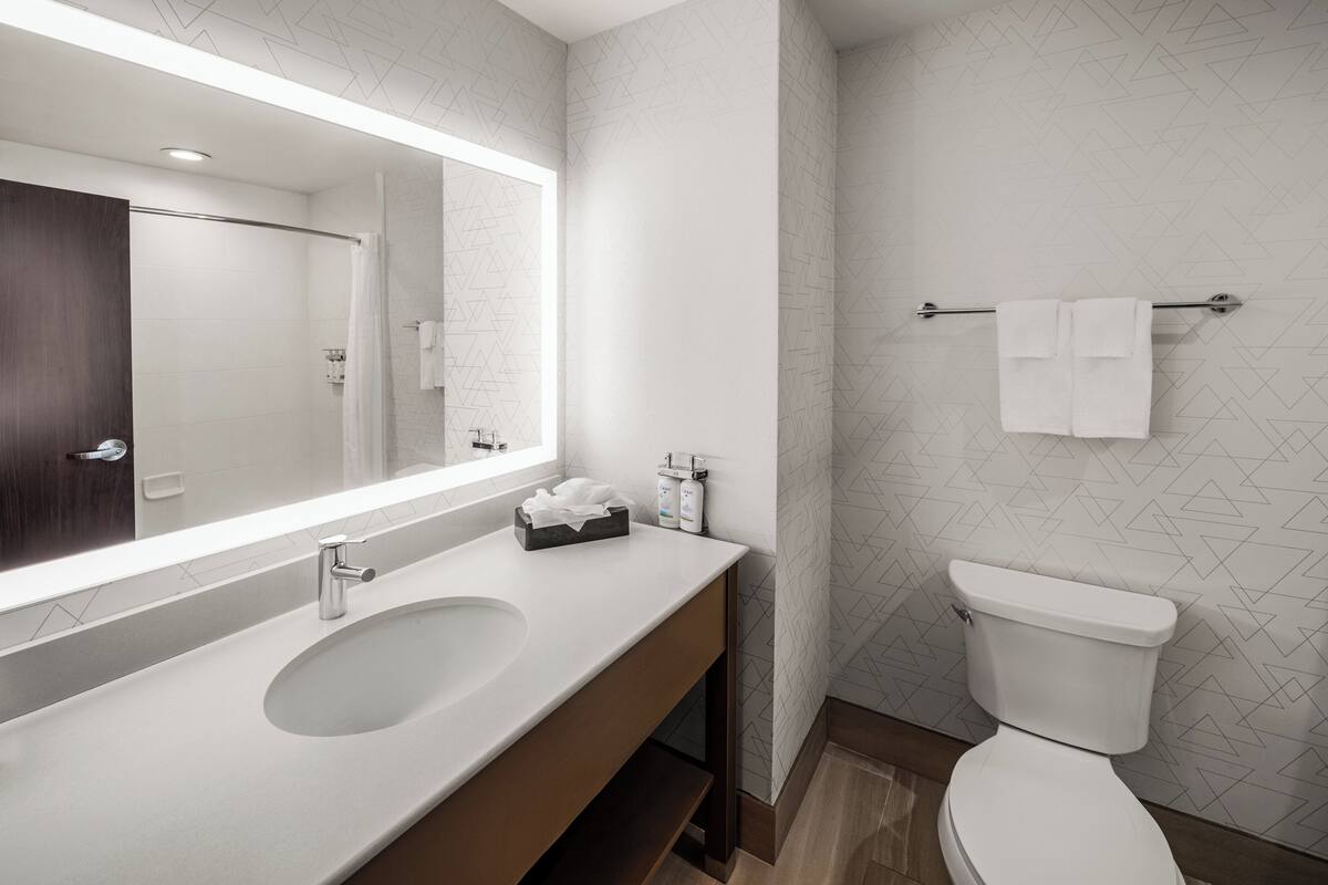 A modern bathroom with a large mirror, two sinks, a toilet, and a towel rack.