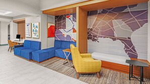 A modern hotel lobby with a sectional sofa, a yellow armchair, a small wooden table, and a large abstract wall mural. - Holiday Inn Express & Suites San Antonio - Frost Bank Ctr (San Antonio)
