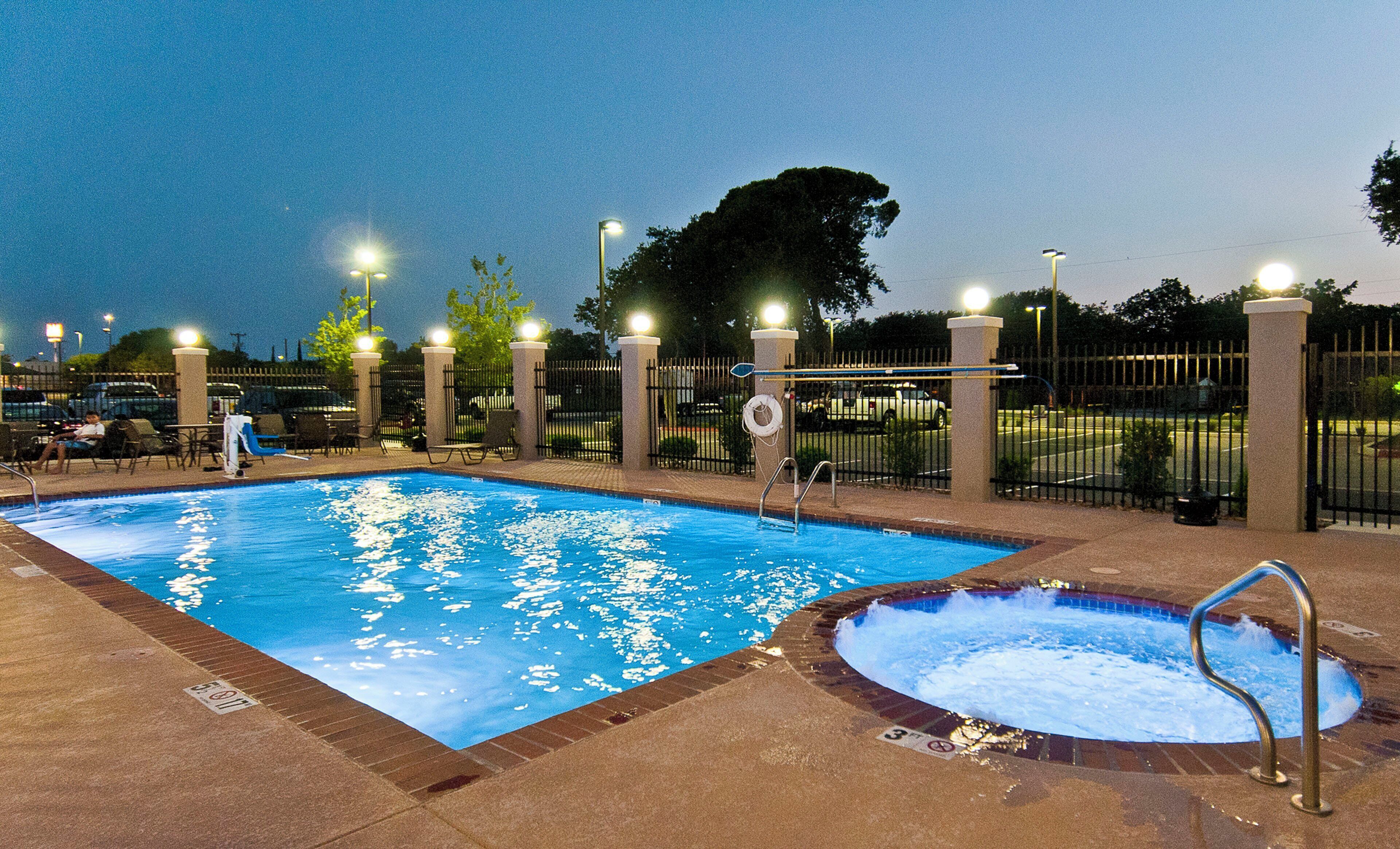 Una piscina con hidromasaje, rodeada de sillas de descanso y una valla.