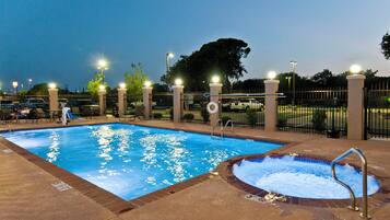 Una piscina con hidromasaje, rodeada de sillas de descanso y una valla.