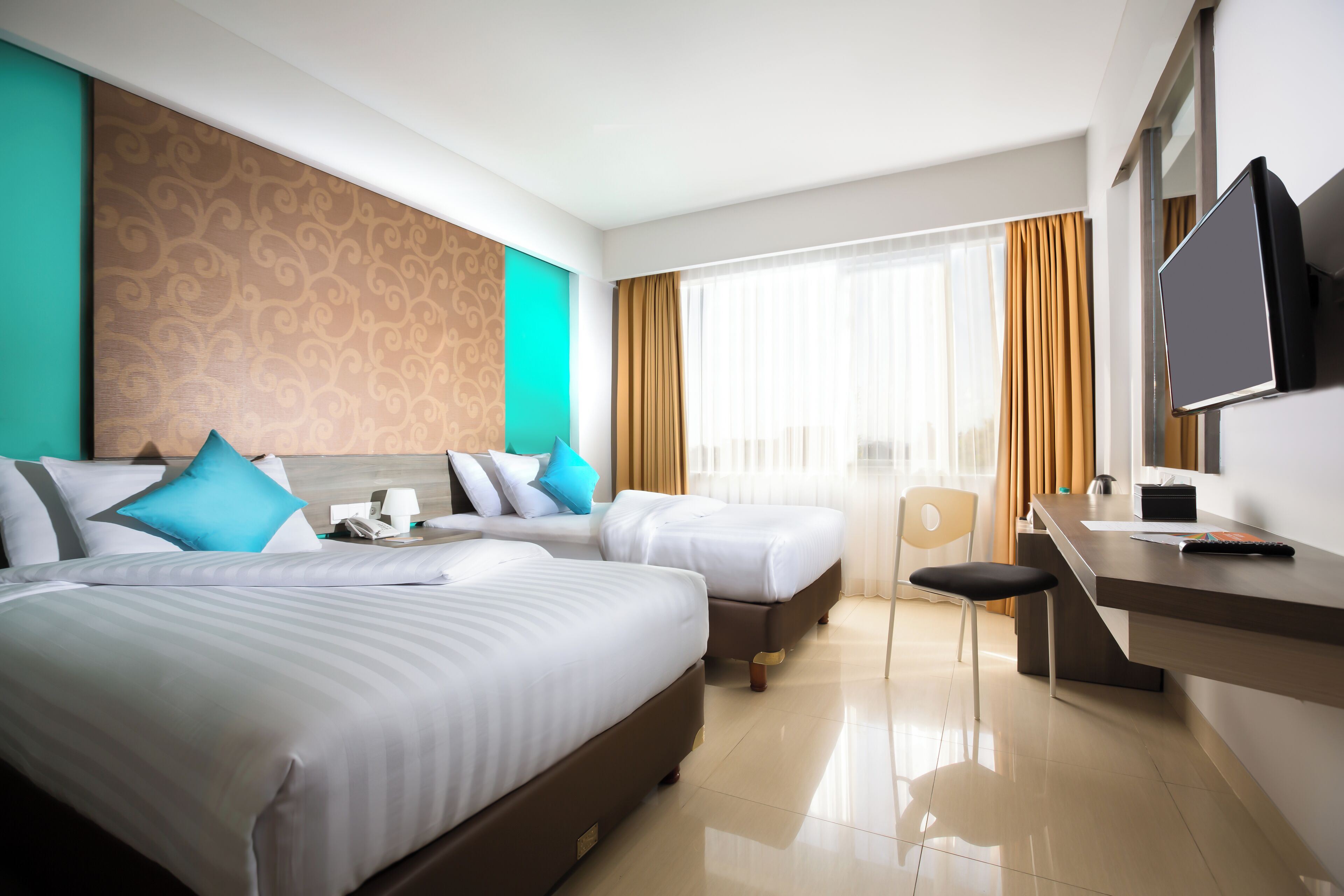 A hotel room with two beds, a desk, a chair, a TV, and a window with curtains.