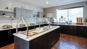 A buffet area with multiple food stations, a glass partition, and a view of the outdoors through a large window. - Staybridge Suites Atlanta Airport by IHG (Atlanta)