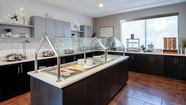 A buffet area with multiple food stations, a glass partition, and a view of the outdoors through a large window. - Staybridge Suites Atlanta Airport by IHG (Atlanta)