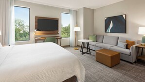 A hotel room with a large bed, a sofa, a coffee table, a TV, and a painting on the wall. - Staybridge Suites Atlanta Airport by IHG (Atlanta)