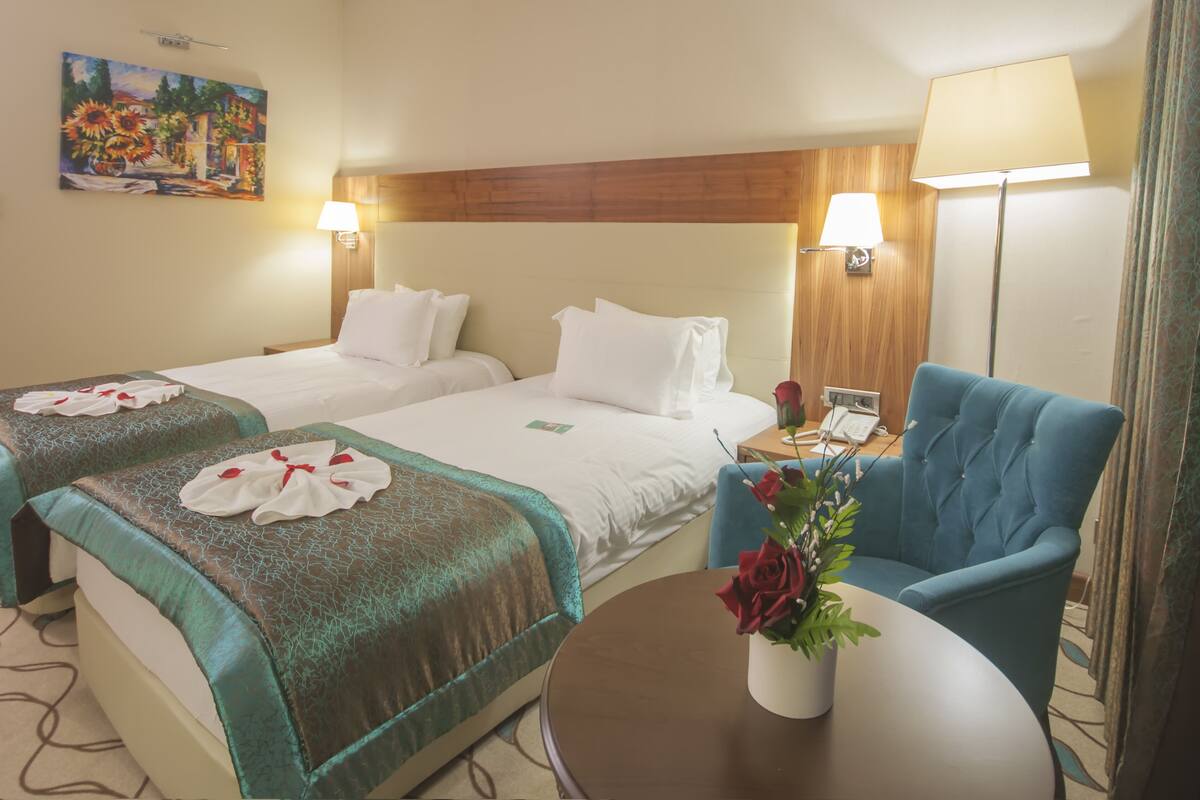 Una habitación de hotel con dos camas, una mesita con un florero y un sillón azul.