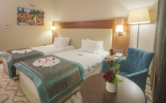 Una habitación de hotel con dos camas, una mesita con un florero y un sillón azul.
