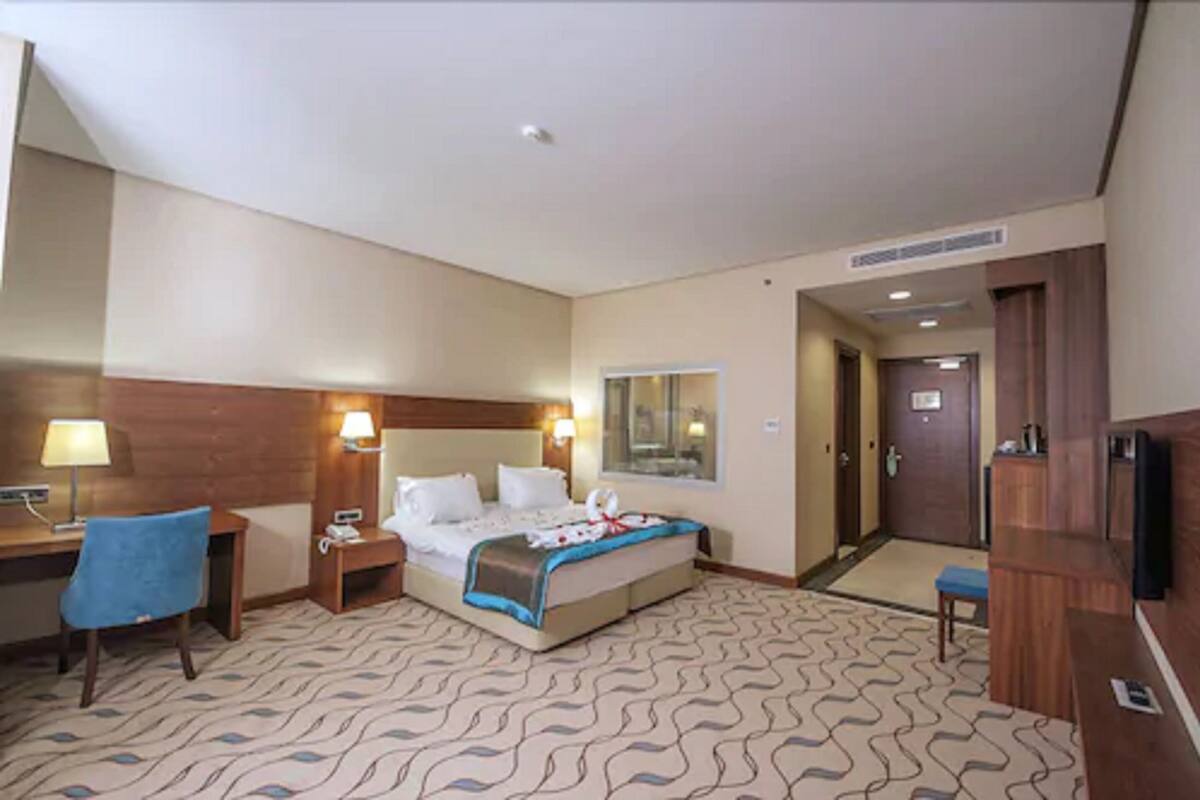 Habitación de hotel con cama, escritorio, silla, televisor y puerta del baño.