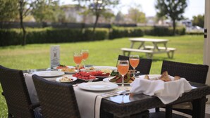 An outdoor dining area with a table set for a meal, surrounded by chairs, and a view of a park with a picnic table in the background. - Margi Hotel (Edirne)