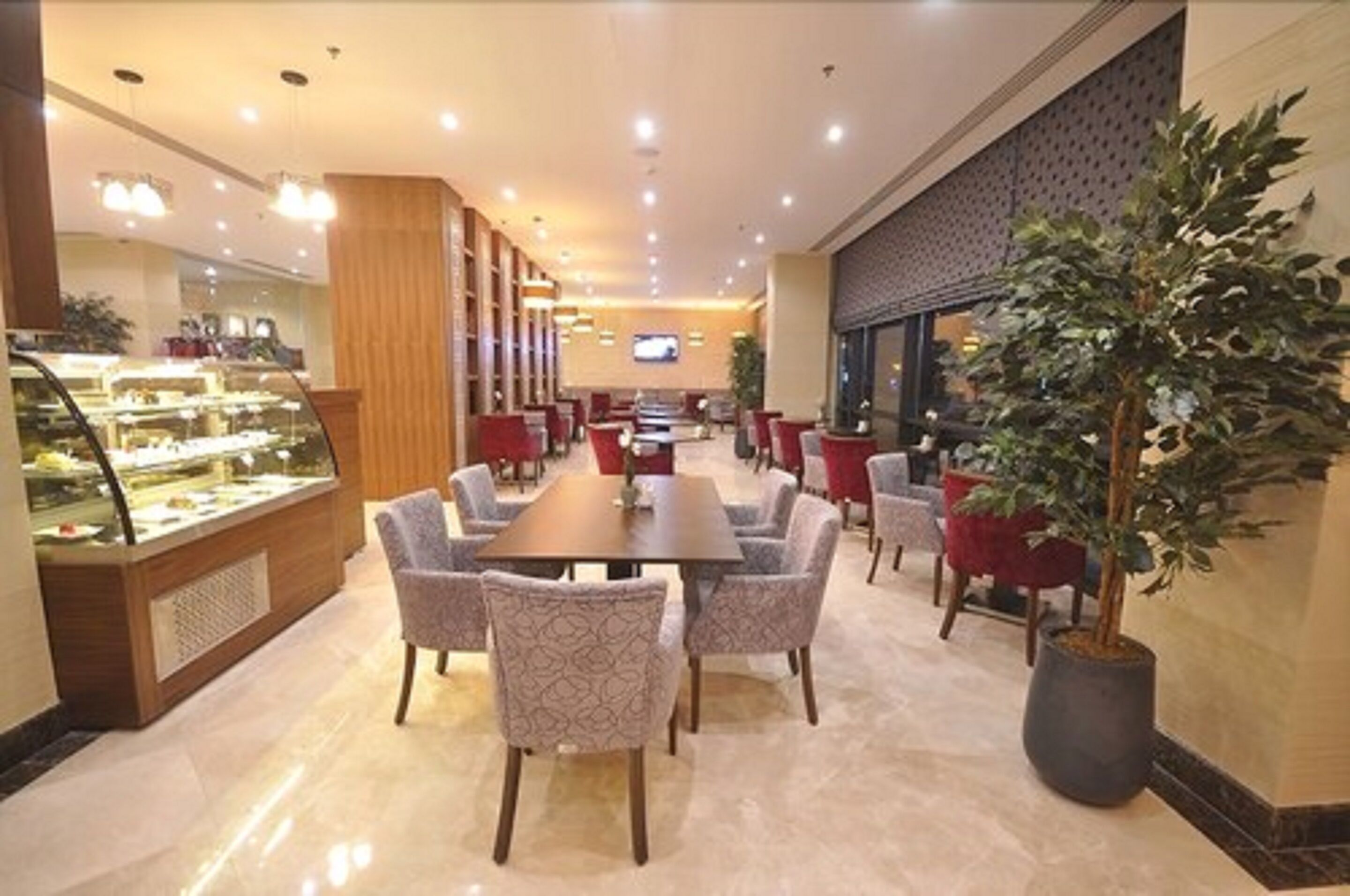 A hotel dining area with a long table, multiple chairs, a dessert display, and a television screen.