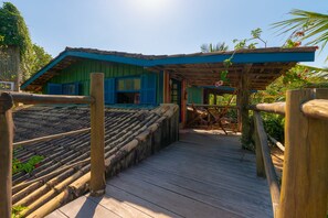 A wooden deck leading to a building with a blue roof and green walls. - Pousada Canto Bravo (Ilhabela)