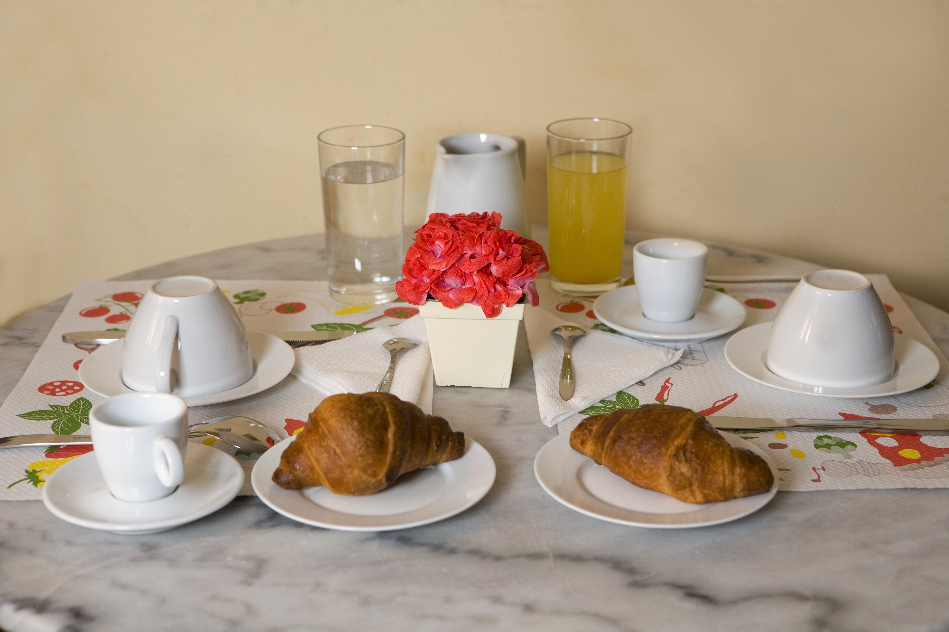 Een ontbijttafel met croissants, kopjes, een karaf en glazen.