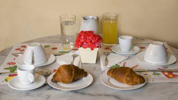 Een ontbijttafel met croissants, kopjes, een karaf en glazen.