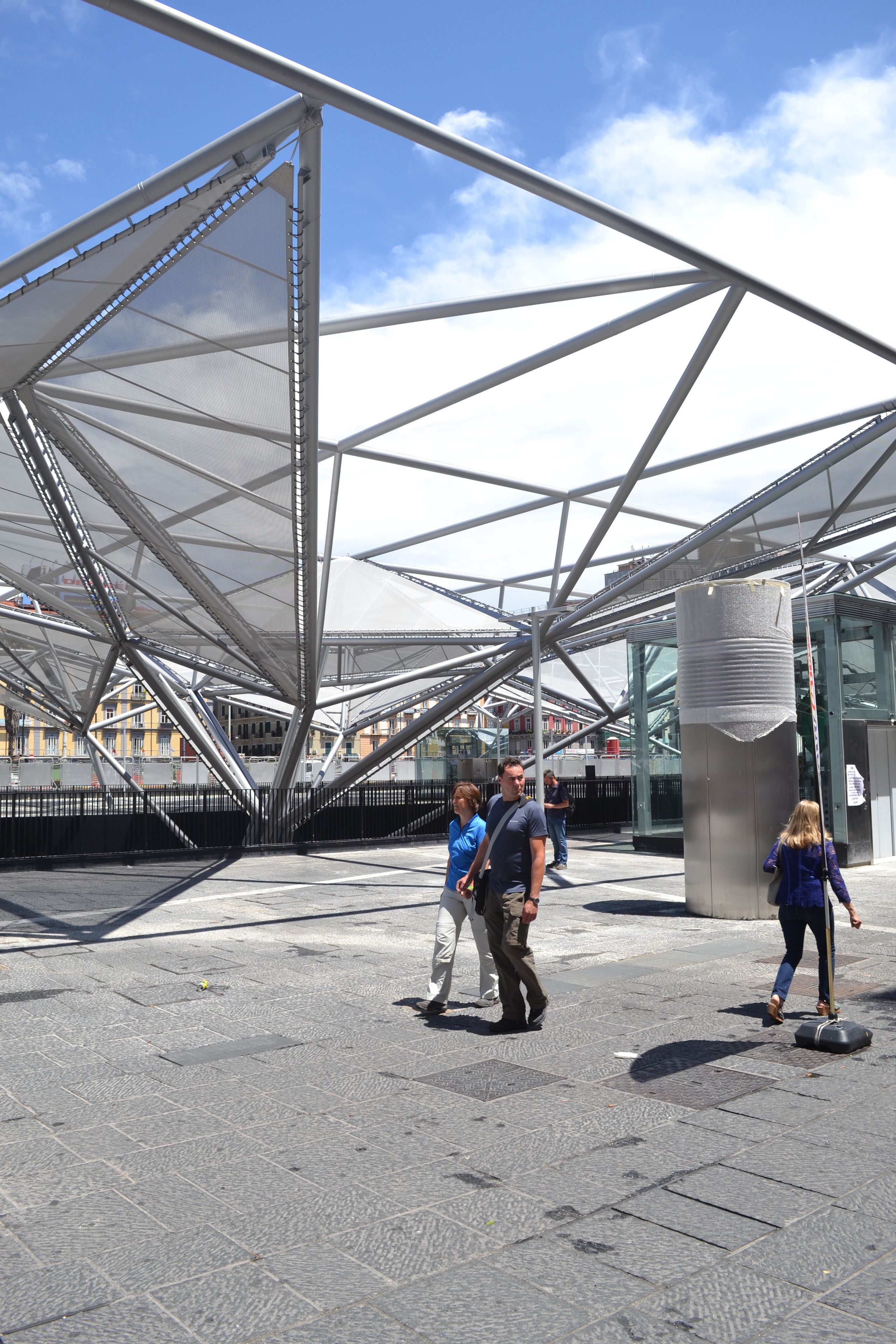 An outdoor area with a modern metal structure and a glass building in the background.