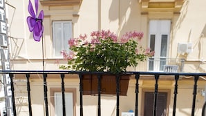 A balcony with two round tables and chairs, a purple pinwheel, and a planter with pink flowers. - Hotel Cine Holiday (Naples)