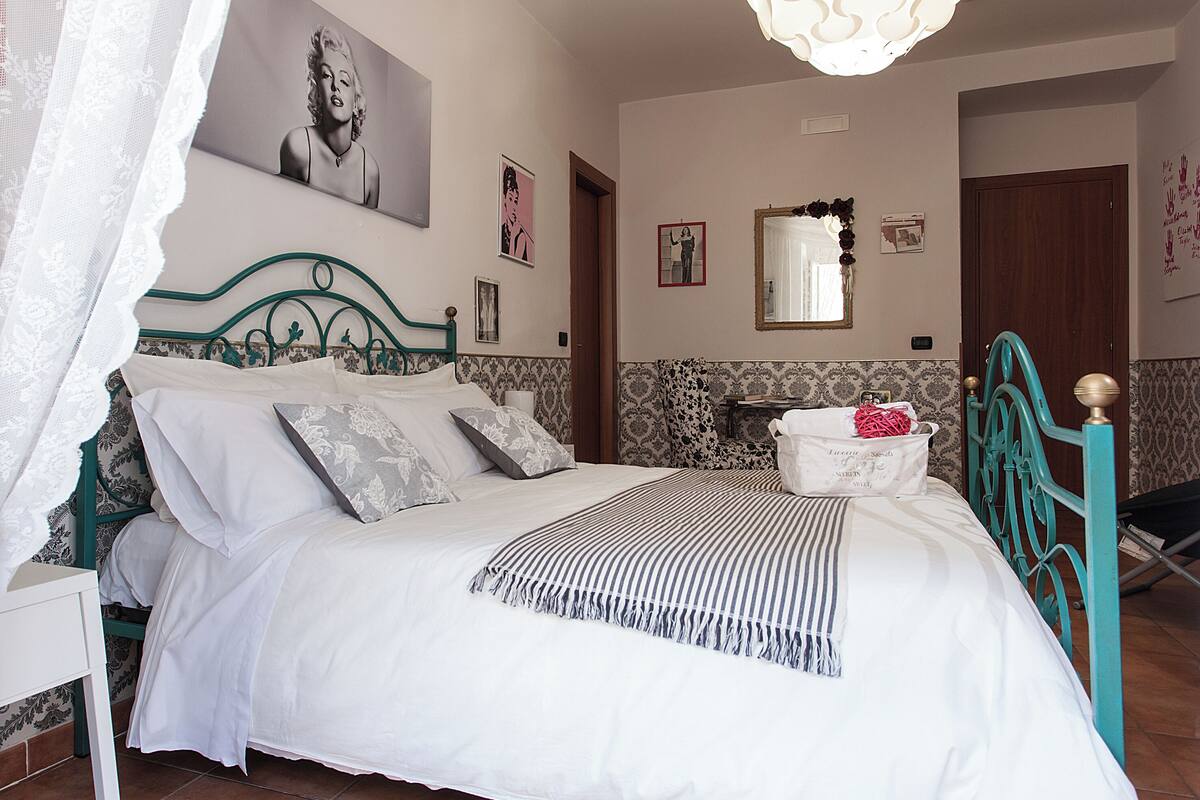 A neatly made bed with a striped blanket, a green metal headboard, and a white nightstand with a lamp.