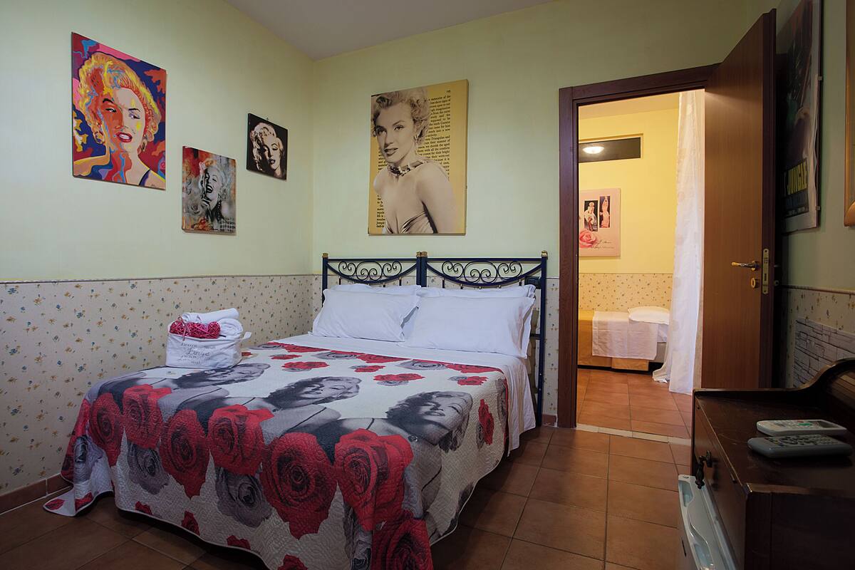 A bedroom with a bed, a bathroom visible through an open door, and various wall art.