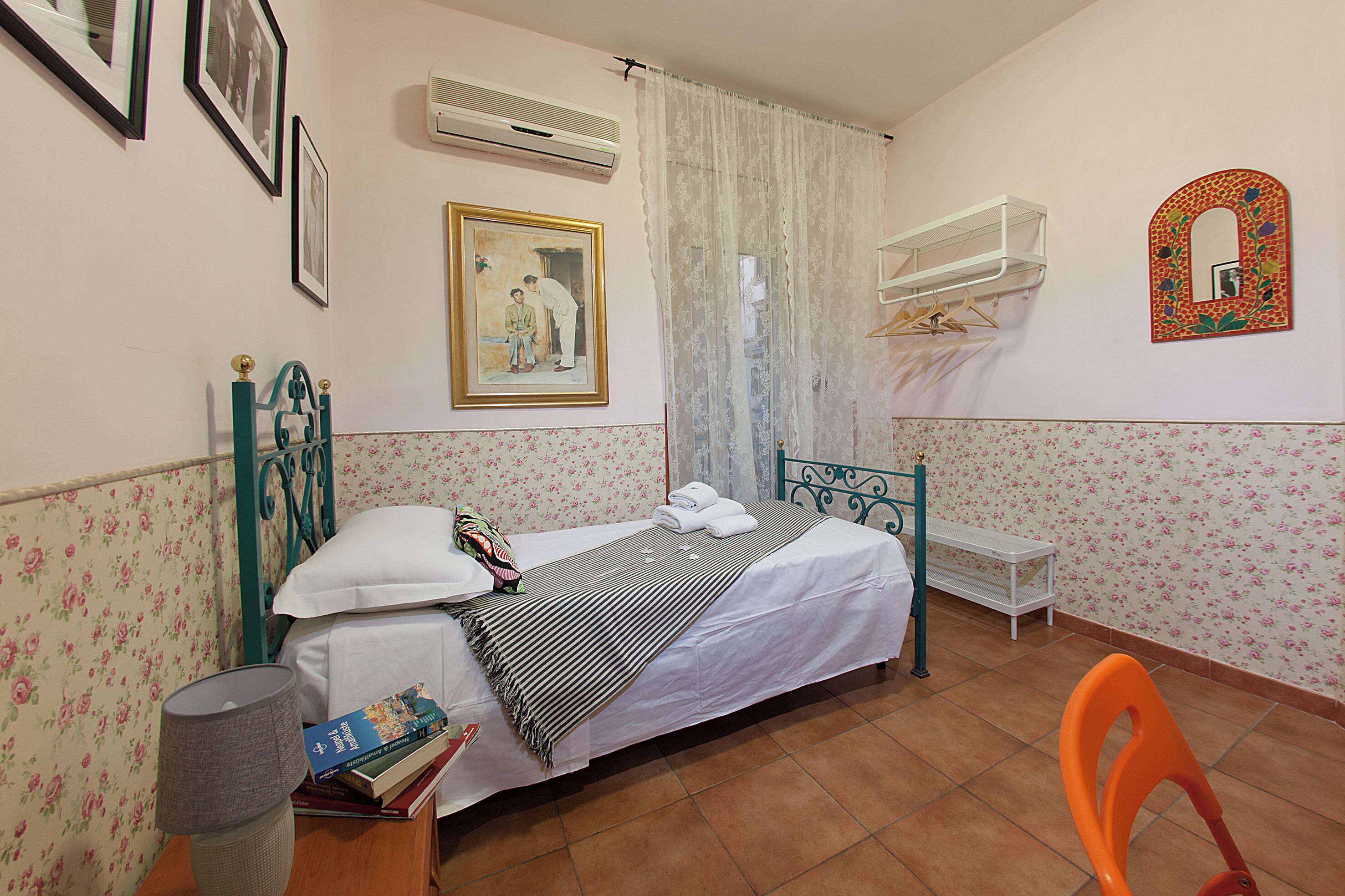 A bedroom with a bed, a bedside table, a chair, a wall-mounted shelf, and a mirror.