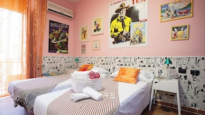 A hotel room with two beds, a small table, and a wall decorated with comic book posters. - Hotel Cine Holiday (Naples)