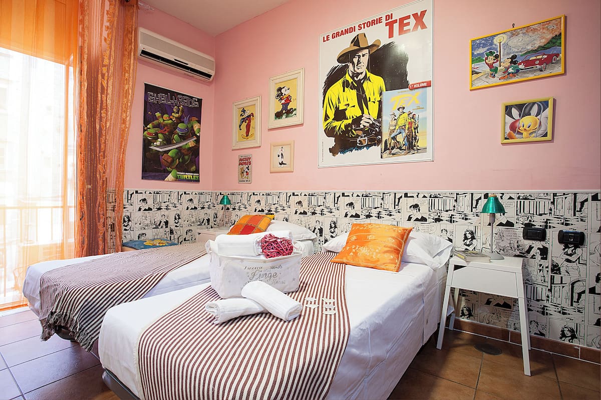 A hotel room with two beds, a small table, and a wall decorated with comic book posters.