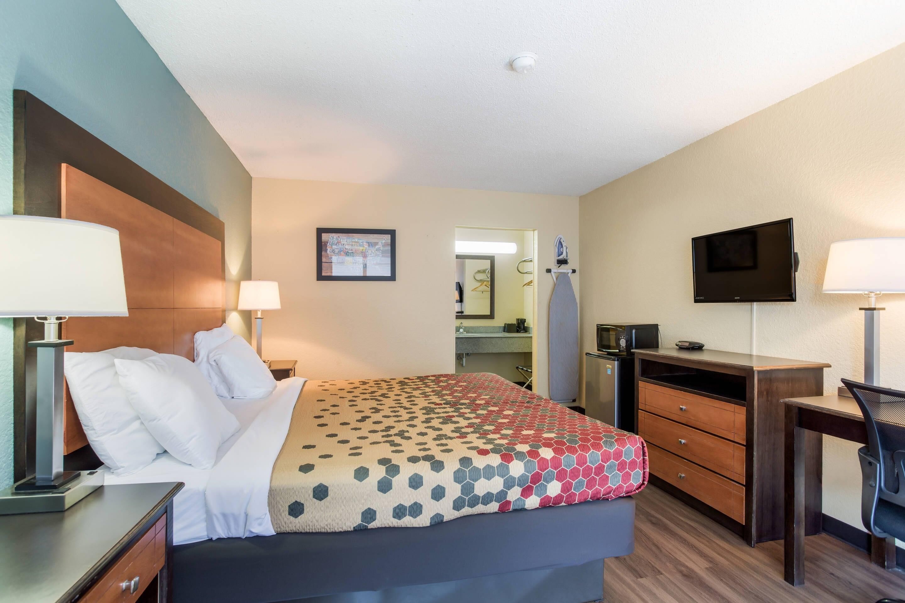 A hotel room with a bed, a desk, a chair, a TV, and a mirror.