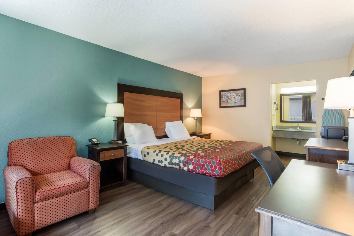 A hotel room with a bed, a desk, a chair, a nightstand, and a mirror.