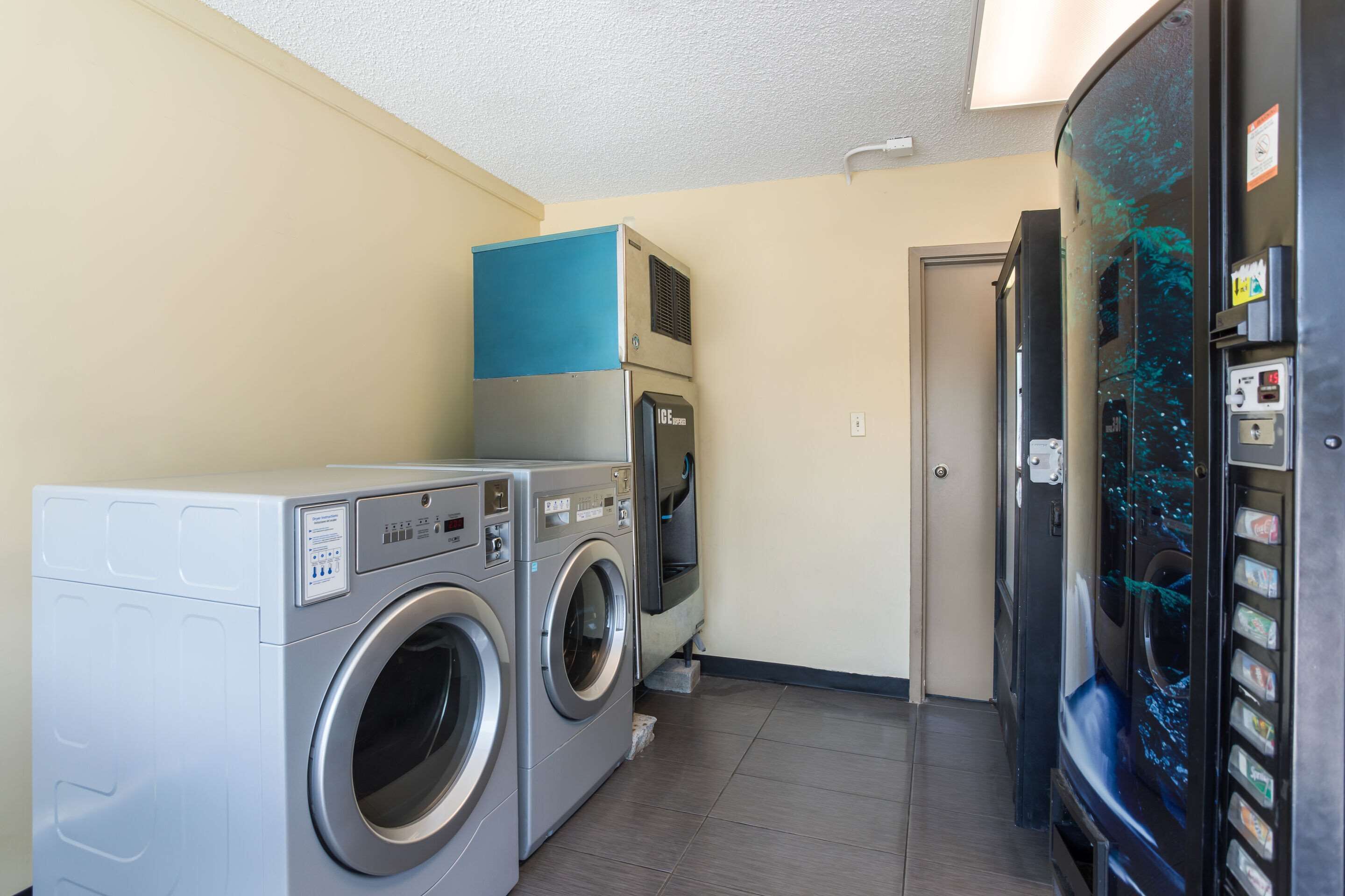 A laundry room with two front-loading washing machines, a dryer, and a vending machine.