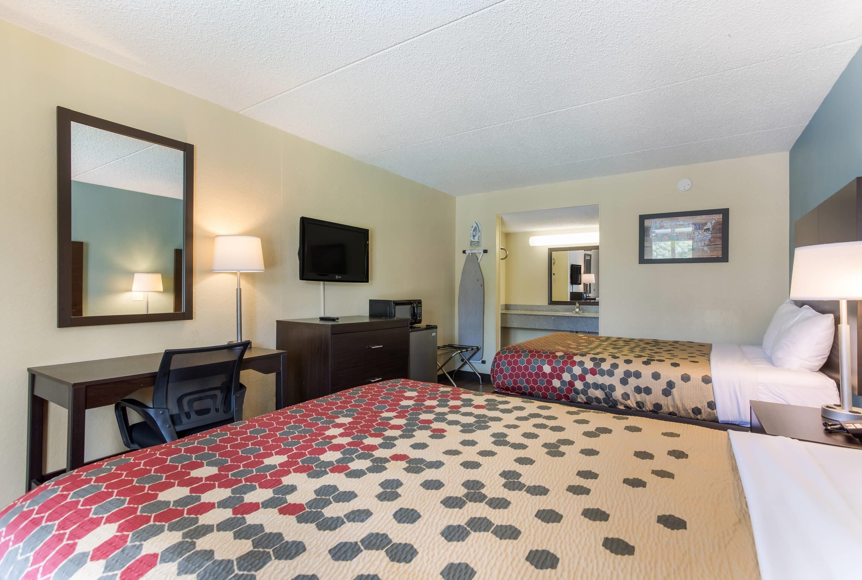 Une chambre d’hôtel avec deux lits, un bureau, une chaise, une télévision et un miroir.