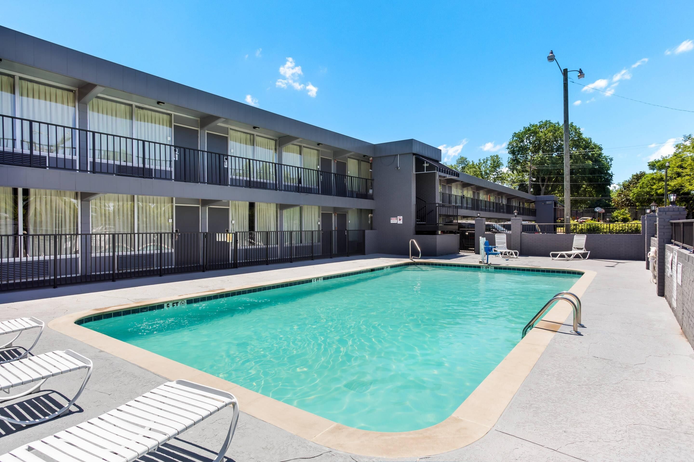 Un hotel con piscina, mobiliario exterior y un edificio de dos pisos con balcones.