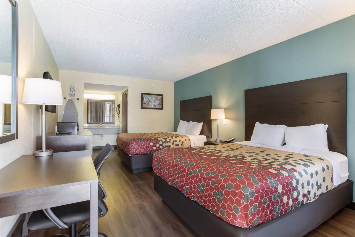 A hotel room with two beds, a desk, a chair, a lamp, and a map on the wall.