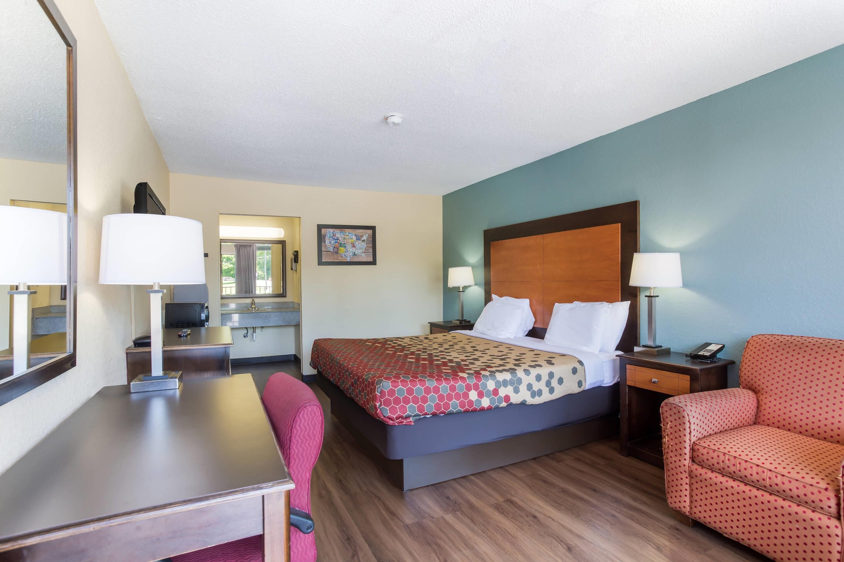 A hotel room with a bed, a desk, a chair, a nightstand, and a mirror.
