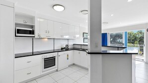 A modern kitchen with white cabinets, a black countertop, and a built-in oven. - White Crest Apartments (Torquay)