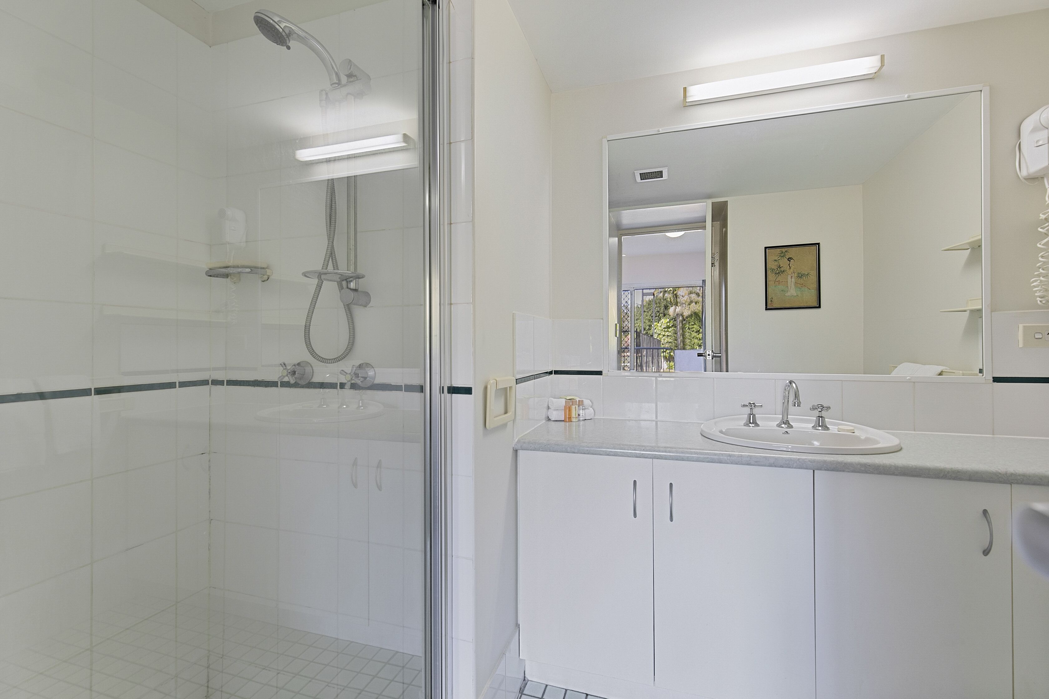 Een moderne badkamer met een douche in een glazen cabine, een witte wastafel en een grote spiegel.