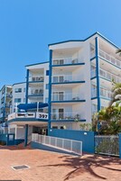 Un hotel de varios pisos con balcones, una zona de recepción y un cartel con la dirección.
