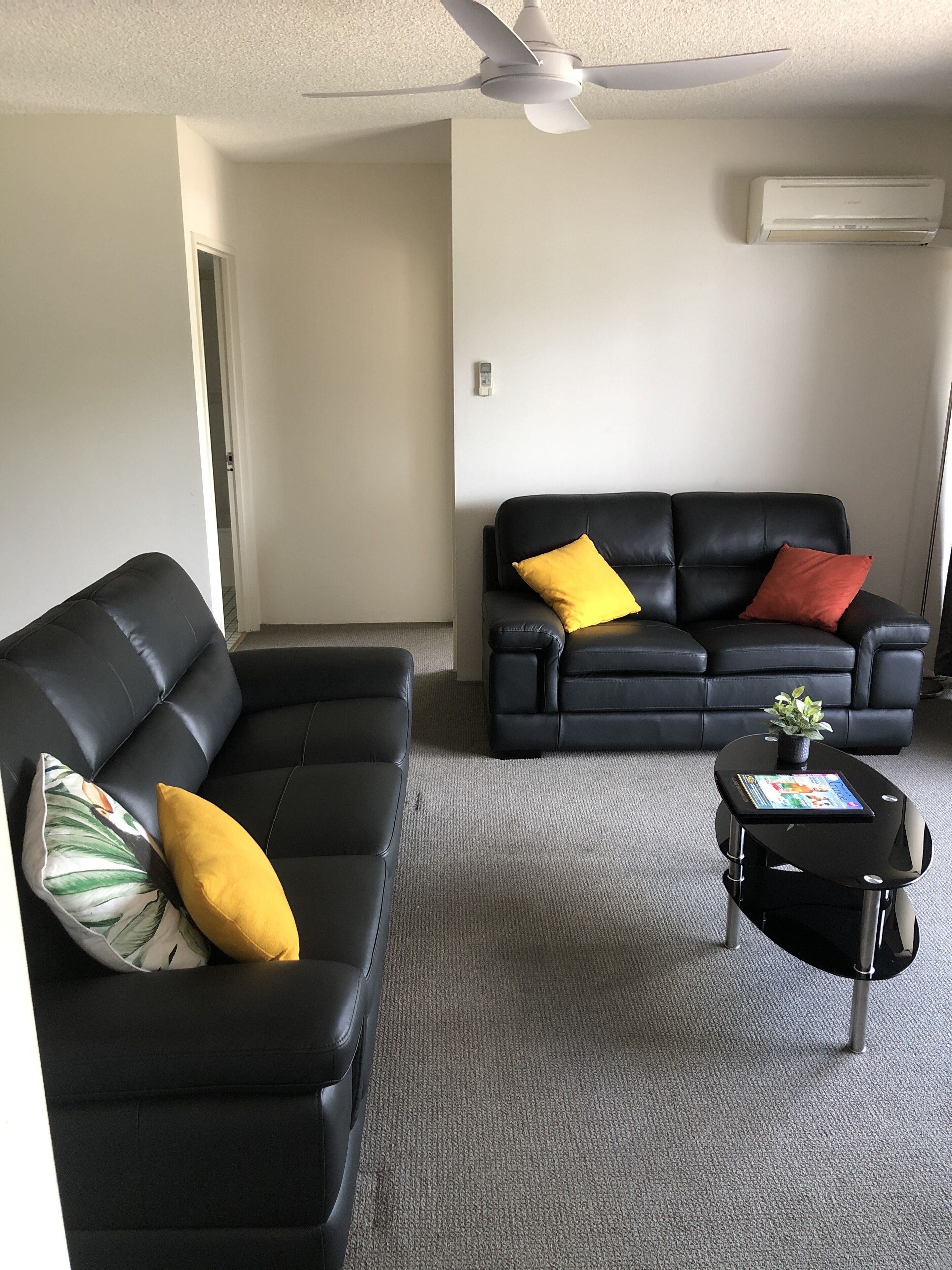 A living room with two black leather sofas, one with a yellow and a striped pillow, and a small black coffee table with a plant.