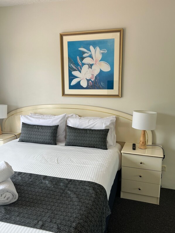 Habitación de hotel ordenada con cama, dos mesitas de noche, una lámpara y un cuadro en la pared.