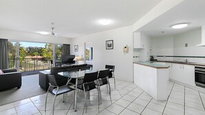 A modern apartment with a dining area, kitchen, and balcony. - White Crest Apartments (Torquay)