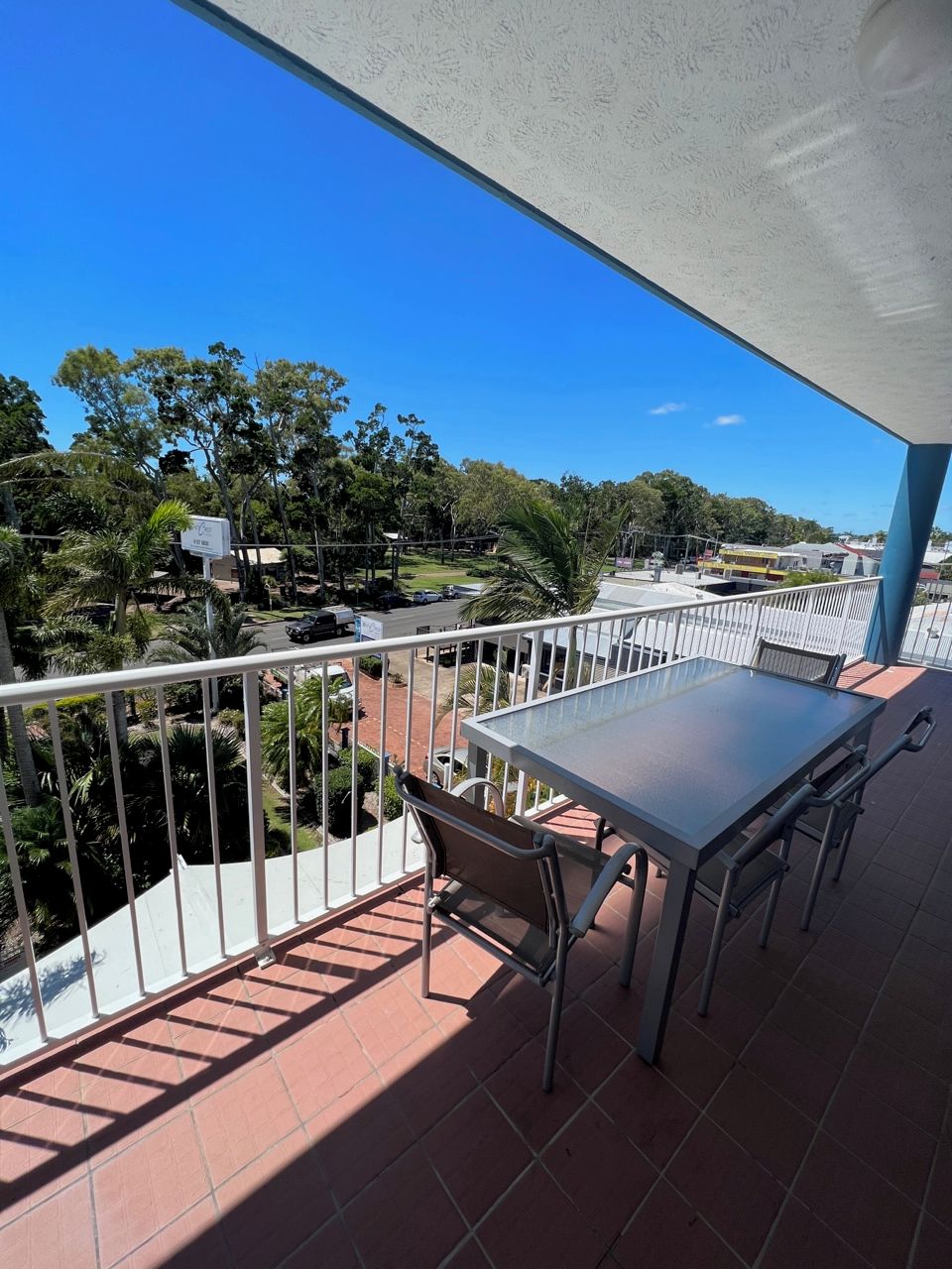 A balcony with a table and chairs, overlooking a parking area and greenery.