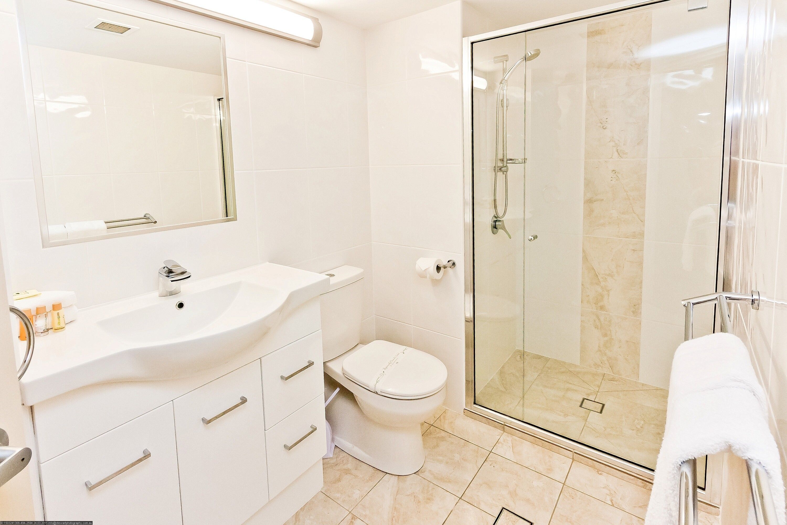 Un baño moderno con ducha envuelta en vidrio, un lavamanos blanco y un inodoro.