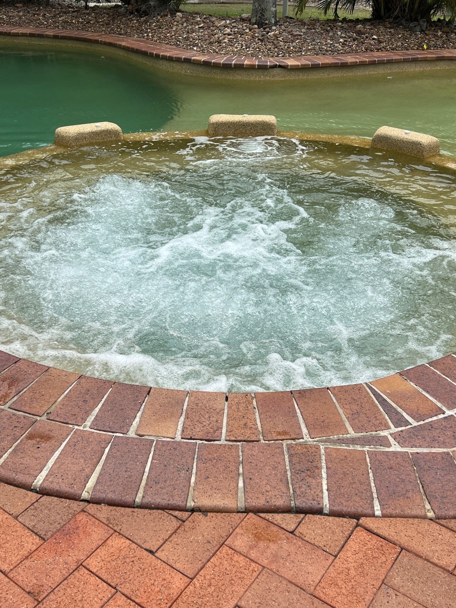 Un jacuzzi con borde de ladrillo y orilla revestida de piedras.