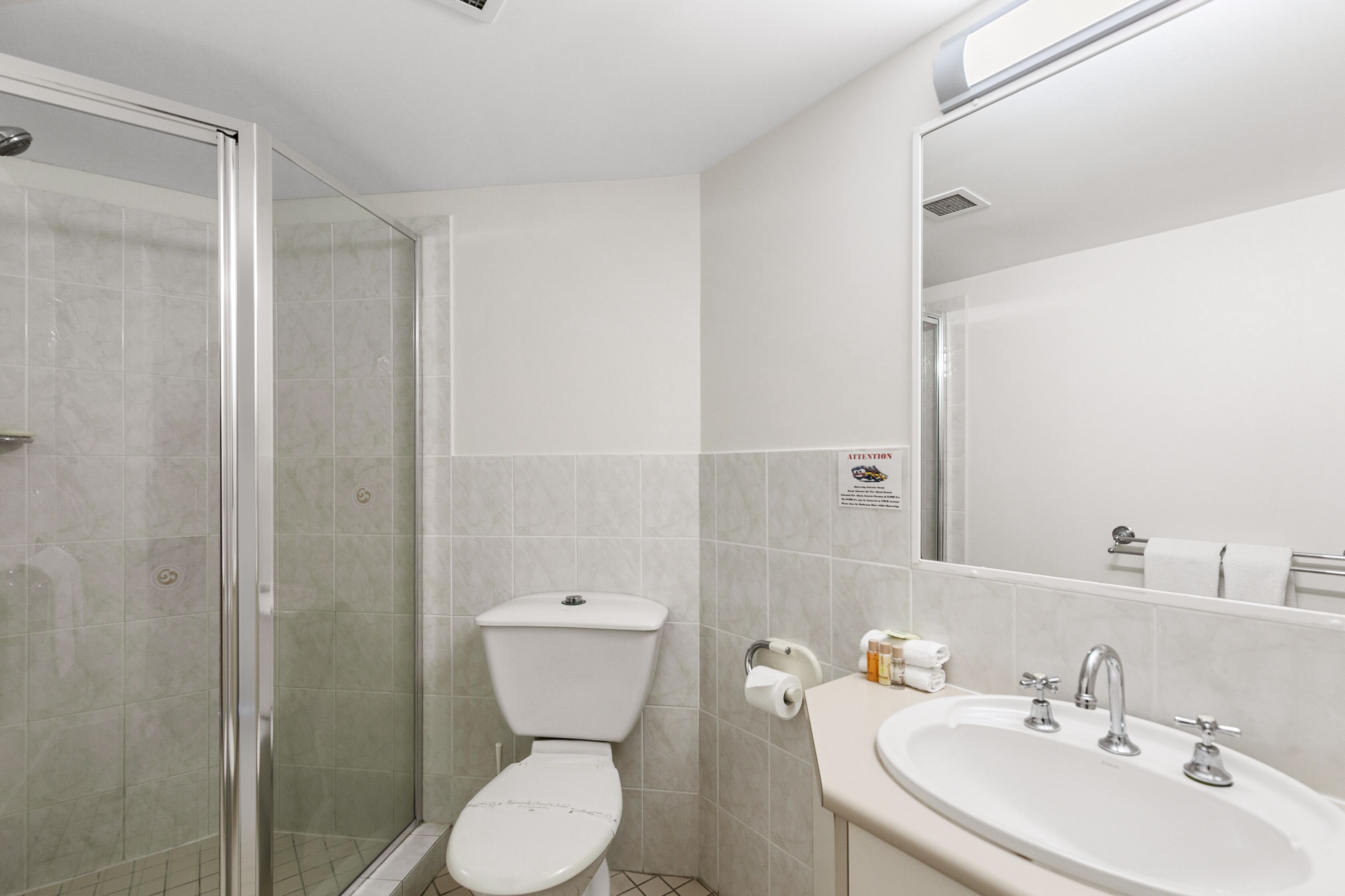 A modern bathroom with a glass shower enclosure, a toilet, and a sink with a mirror above it.