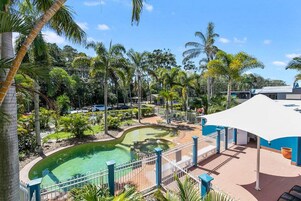 Zona de piscina con diseño curvo, rodeada de palmeras y una estructura blanca tipo dosel.