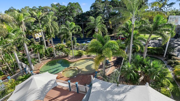 A view of a golf course with a putting green, surrounded by palm trees and a white tent-like structure. - White Crest Apartments (Torquay)